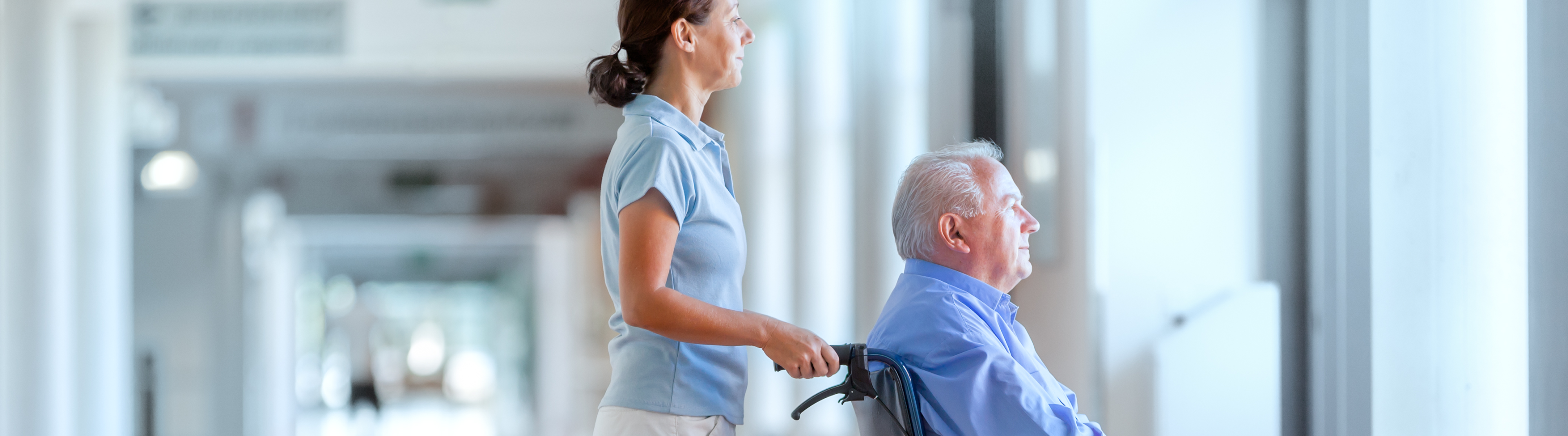 Female pushing older man in wheelchair in hospital setting