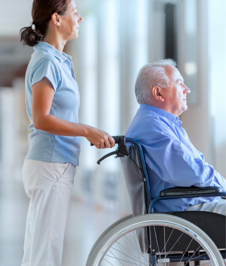 Female pushing older man in wheelchair in hospital setting
